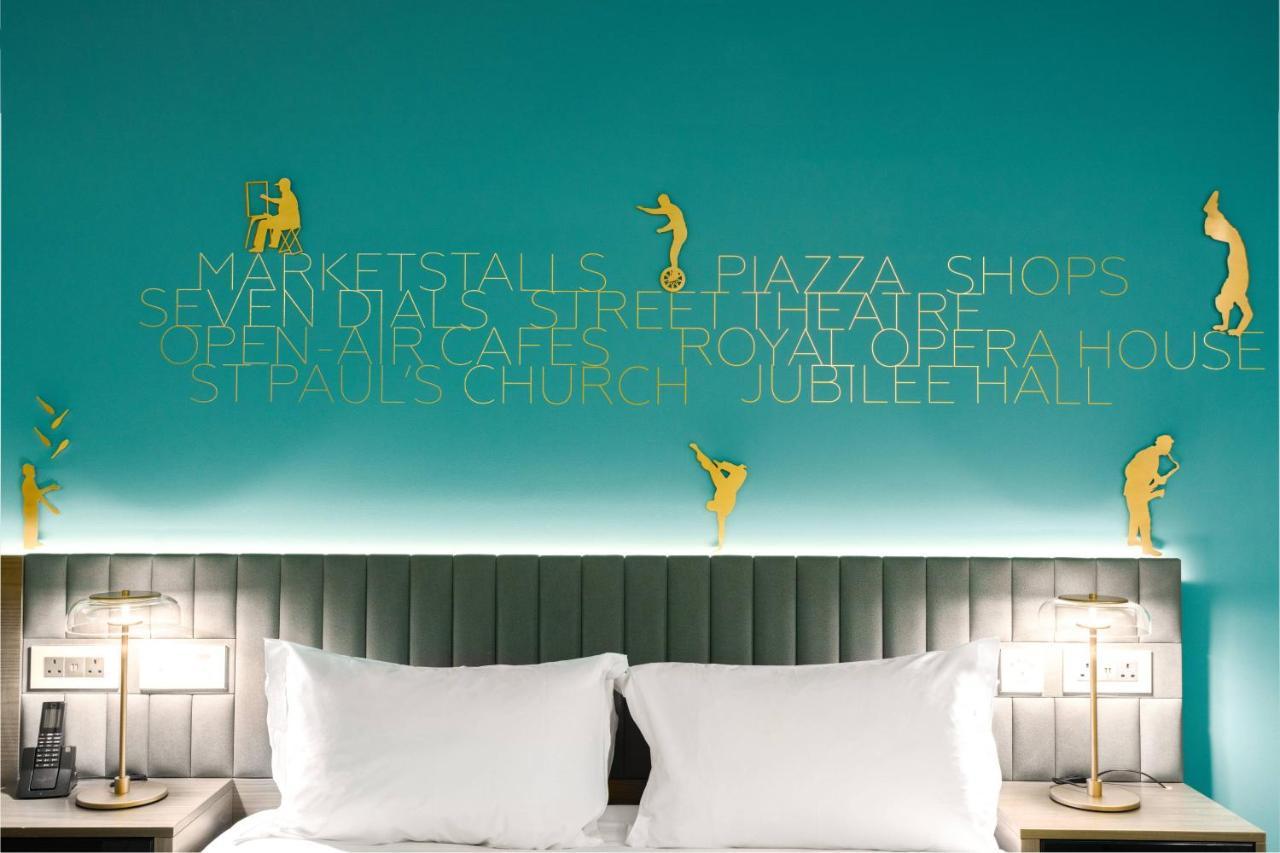 Middle Eight - Covent Garden - Preferred Hotels And Resorts 런던 외부 사진 The photo shows a modern hotel room with a distinctive turquoise wall. On the wall, there are gold silhouettes of people engaged in various activities, suggesting movement or leisure. The wall also features text that highlights local attractions like