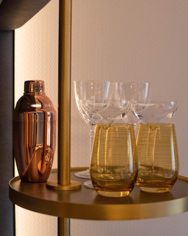 Middle Eight - Covent Garden - Preferred Hotels And Resorts 런던 외부 사진 The photo shows a stylish bar setup featuring a shiny copper cocktail shaker positioned next to several elegant glassware pieces. There are four tall, clear stemmed glasses and two round, amber-colored glasses with a textured pattern. The background 