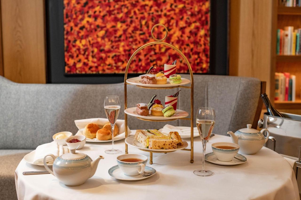 Middle Eight - Covent Garden - Preferred Hotels And Resorts 런던 외부 사진 The photo shows an elegant afternoon tea setup on a white tablecloth. At the center, there is a multi-tiered stand displaying a variety of pastries and desserts, including cakes and colorful sweets. Surrounding the stand are teapots and teacups, read
