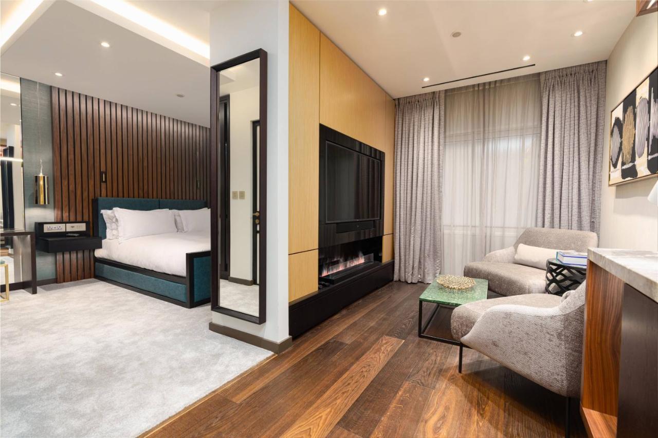 Middle Eight - Covent Garden - Preferred Hotels And Resorts 런던 외부 사진 The photo depicts a modern hotel room or suite featuring a cozy living space. On one side, there's a comfortable bed with plush bedding, positioned against a backdrop of elegant wooden paneling. Adjacent to the bed is a contemporary fireplace integra