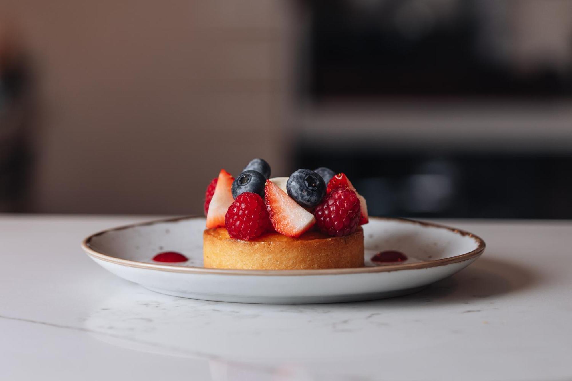 Middle Eight - Covent Garden - Preferred Hotels And Resorts 런던 외부 사진 The photo shows a delicious-looking dessert on a white plate. The dessert appears to be a small tart or cake topped with fresh strawberries, raspberries, and blueberries. It has a golden crust, and there are small dollops of a red sauce or fruit pure