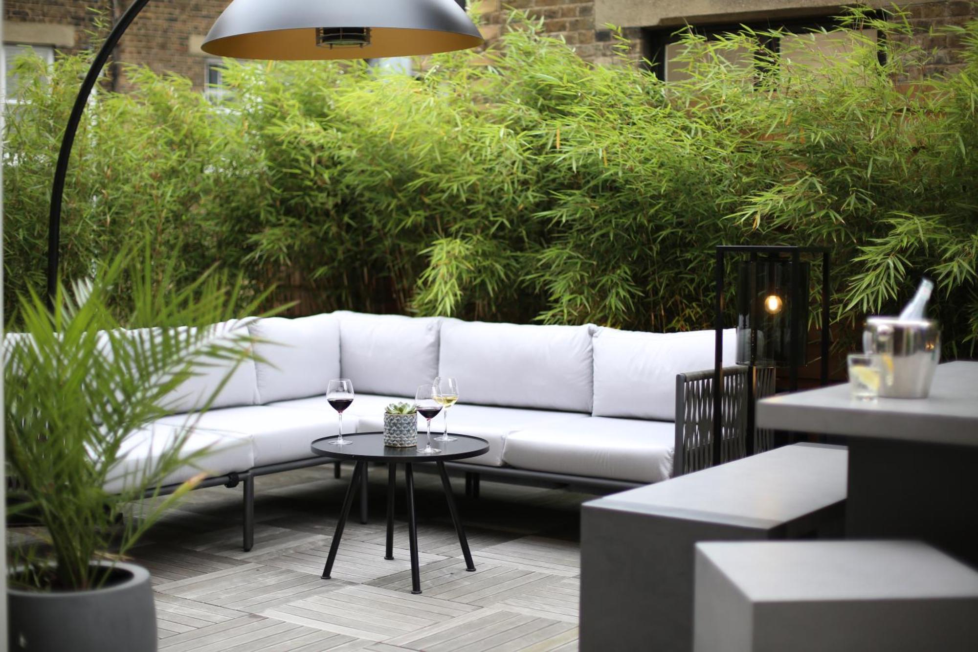 Middle Eight - Covent Garden - Preferred Hotels And Resorts 런던 외부 사진 The photo shows an outdoor seating area featuring a modern gray sectional sofa with plush cushions. In front of the sofa is a small, round black table with two glasses of wine on it, accompanied by a decorative plant or vase. Surrounding the area are